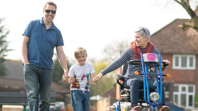A woman living with LGMD and who uses a mobility scooter holds hands with her son while her husband holds his other hand