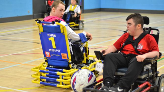 Two wheelchair football players both lock on eyes on the ball between them.