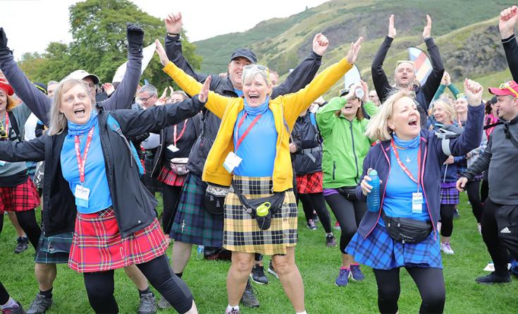 Crowd of people wearing kilts, laughing with their arms in the air