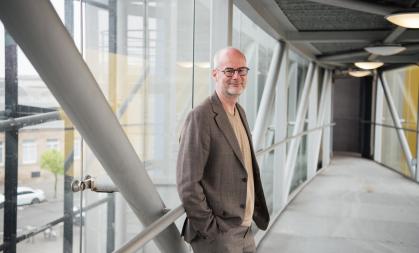 Professor Volker Straub standing in a windowed hallway, smiling at the camera